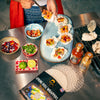 Person preparing spring roll appetizers with ingredients on a table, including a box of SIAM spring roll wrappers and sauces.