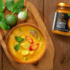 Yellow Thai curry in a bowl with curry paste jar on a wooden surface